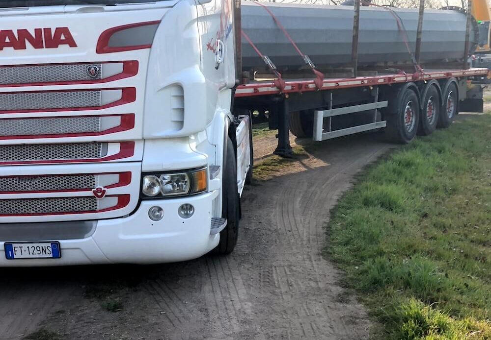 Camion per carichi speciali trasporta tubature su una strada sterrata.